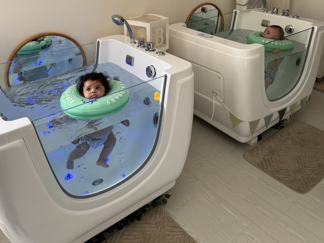 Duas banheiras de baby spa na sala partilhada, cada uma com um bebé a flutuar
